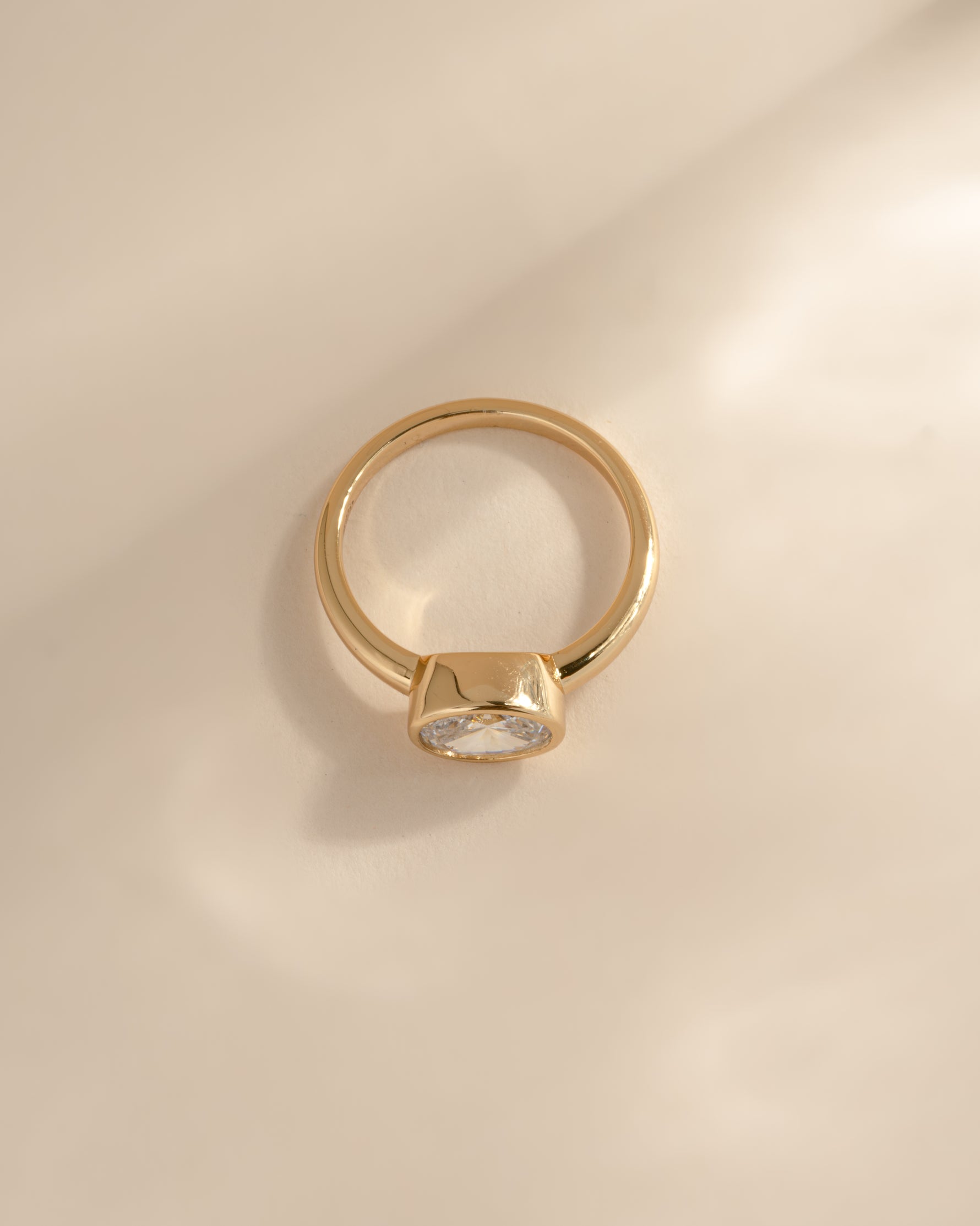 A side profile of a  gold ring with a bezel-set cz stone, photographed on a warm beige background with soft shadows.