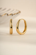 Gold oval hoop earrings from Sami Jewels shown in an angled view, highlighting their smooth, elegant design.