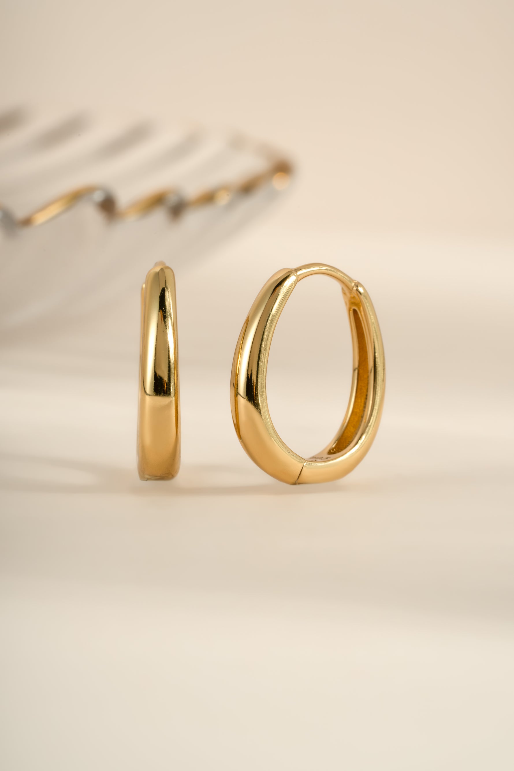 Gold oval hoop earrings from Sami Jewels shown in an angled view, highlighting their smooth, elegant design.