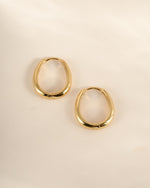 Gold oval hoop earrings from Sami Jewels shown in a side profile view, highlighting their smooth, rounded design.