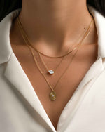 Gold oval medallion necklace by Sami Jewels worn on a model, showcasing elegant jewelry design with intricate details.