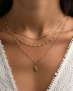 Gold oval medallion necklace from Sami Jewels worn layered on a model with a simple chain design.
