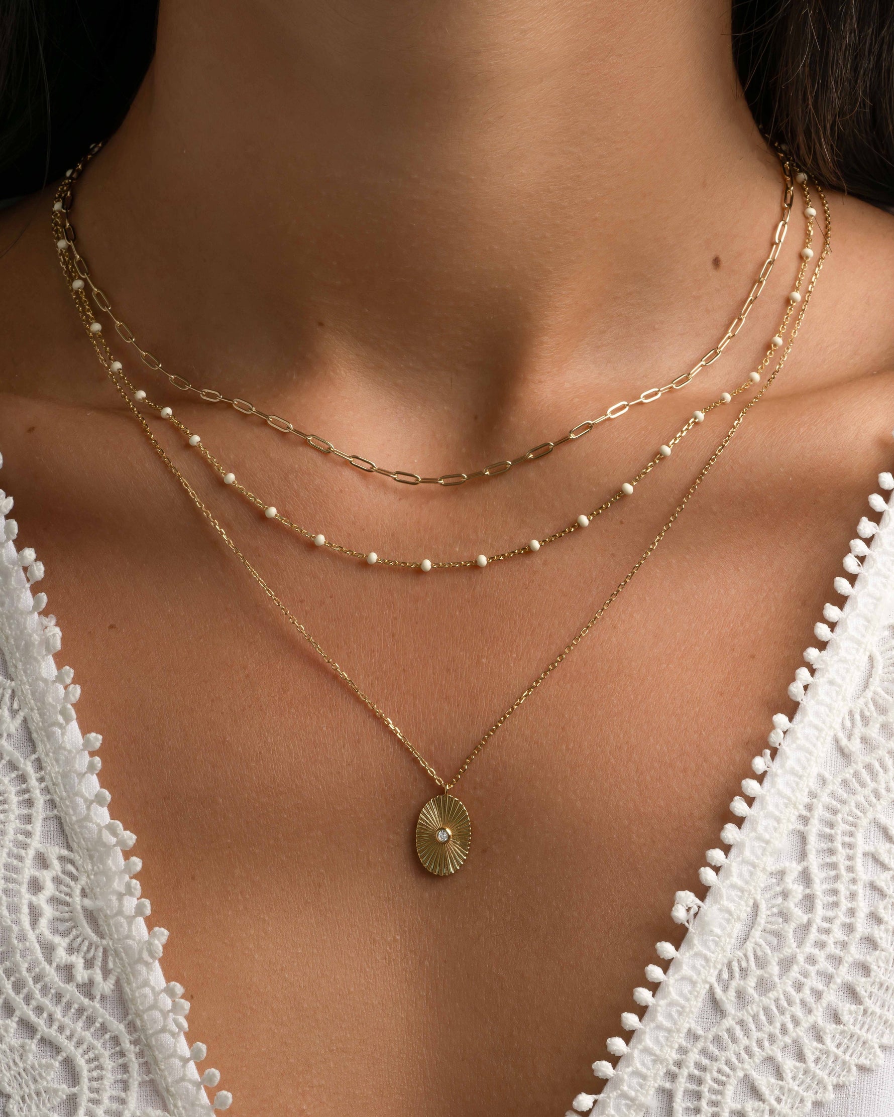 Gold oval medallion necklace from Sami Jewels worn layered on a model with a simple chain design.