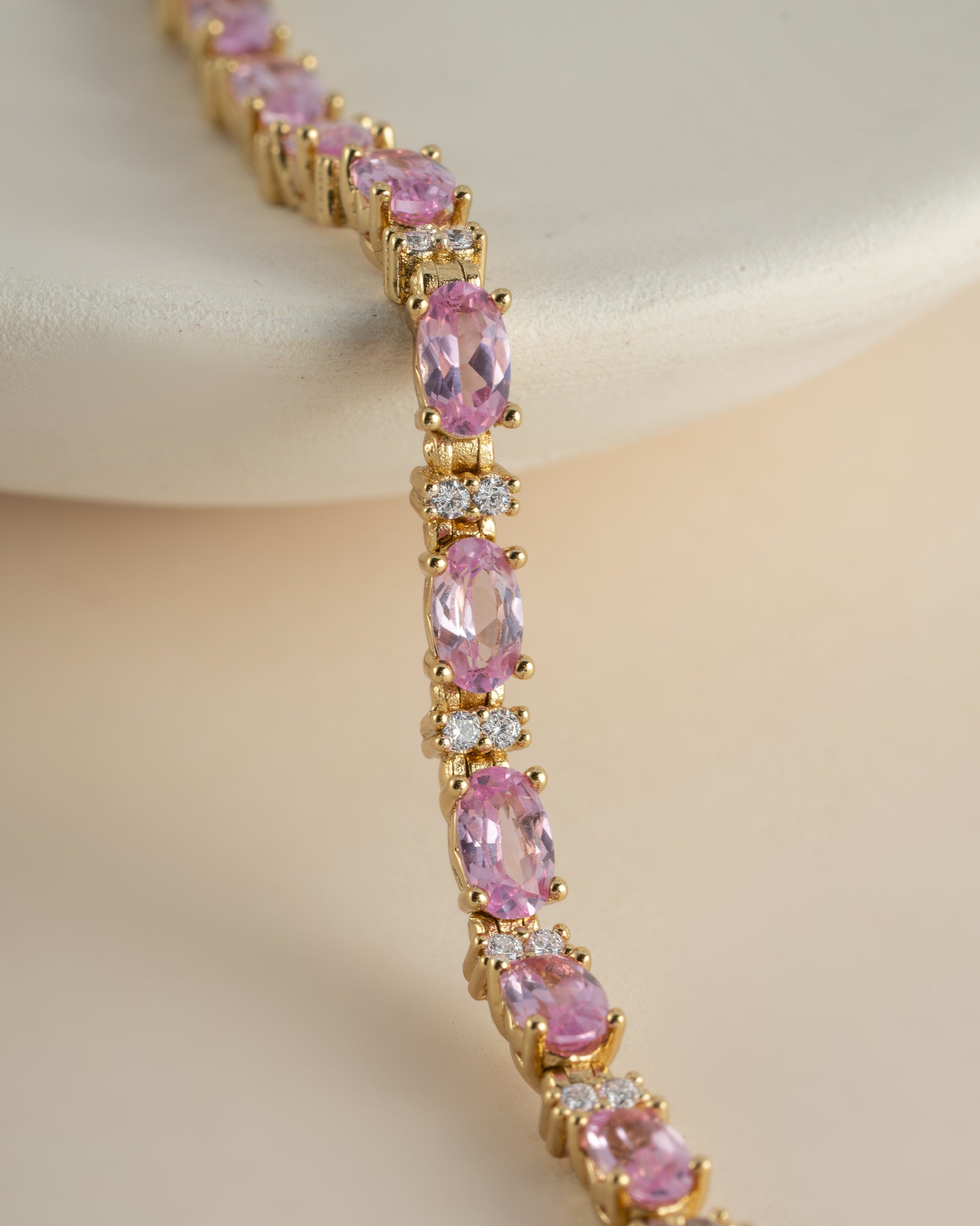 Gold tennis bracelet with oval pink gemstones and round white diamonds.