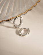 Close-up of Sami Jewels oval plain sterling silver huggie earrings showing smooth, minimalist design on a white background.
