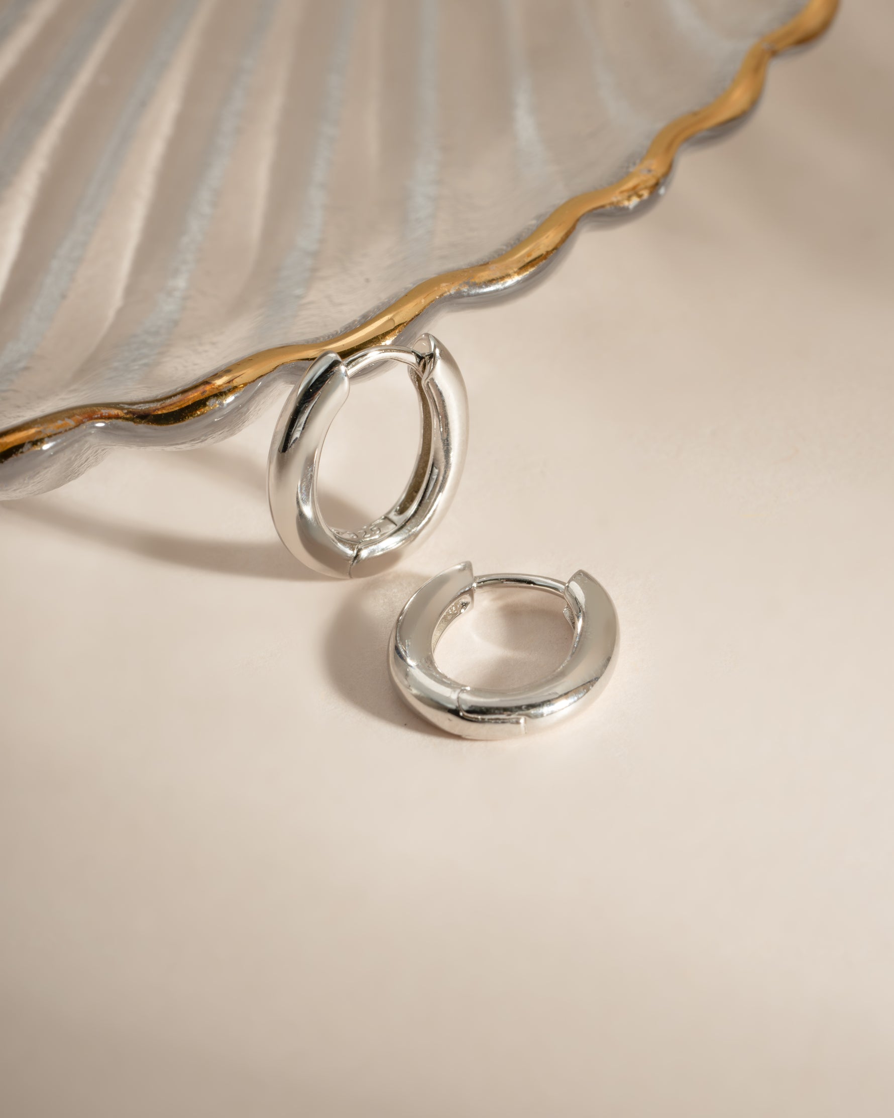 Close-up of Sami Jewels oval plain sterling silver huggie earrings showing smooth, minimalist design on a white background.