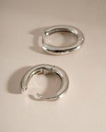 Close-up of sterling silver oval plain huggie earrings by Sami Jewels, showcasing their simple, elegant hoop design.