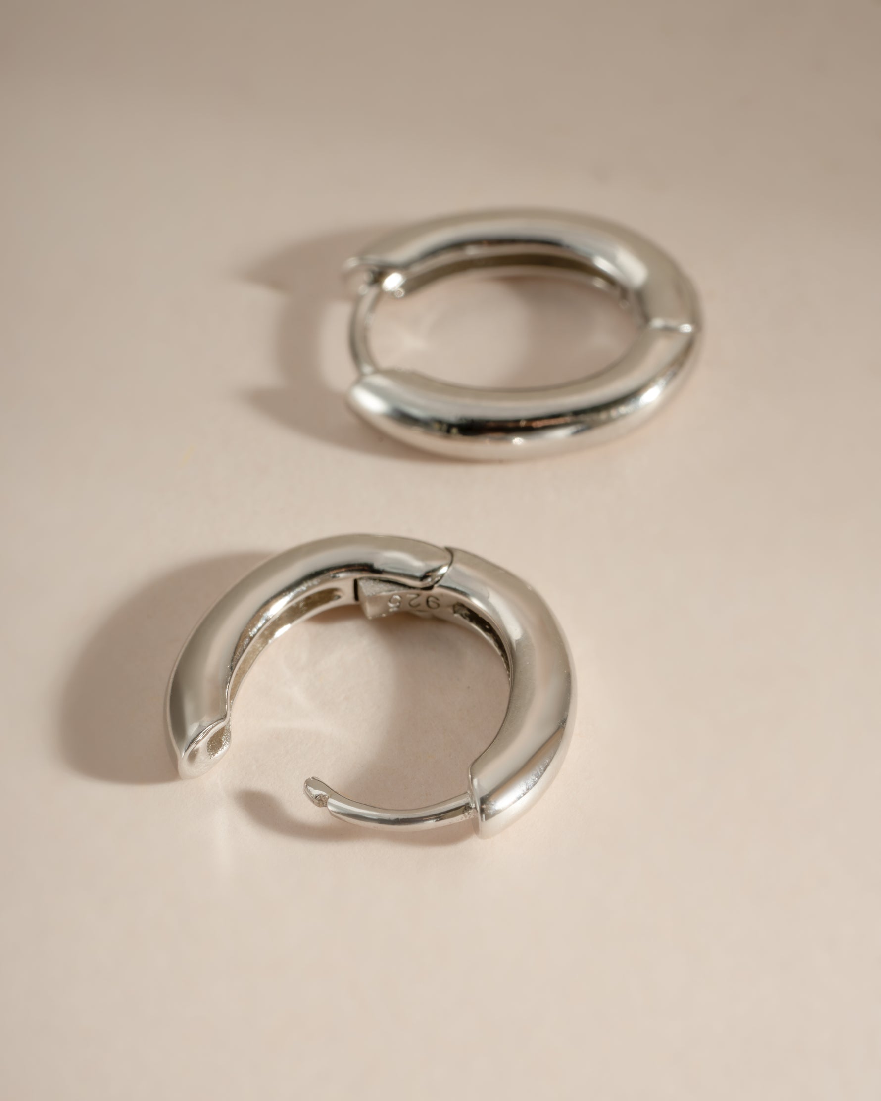 Close-up of sterling silver oval plain huggie earrings by Sami Jewels, showcasing their simple, elegant hoop design.