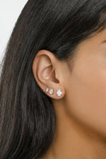 Three oval studs, including the 6x8mm size, stacked on a dark-haired model's ear.
