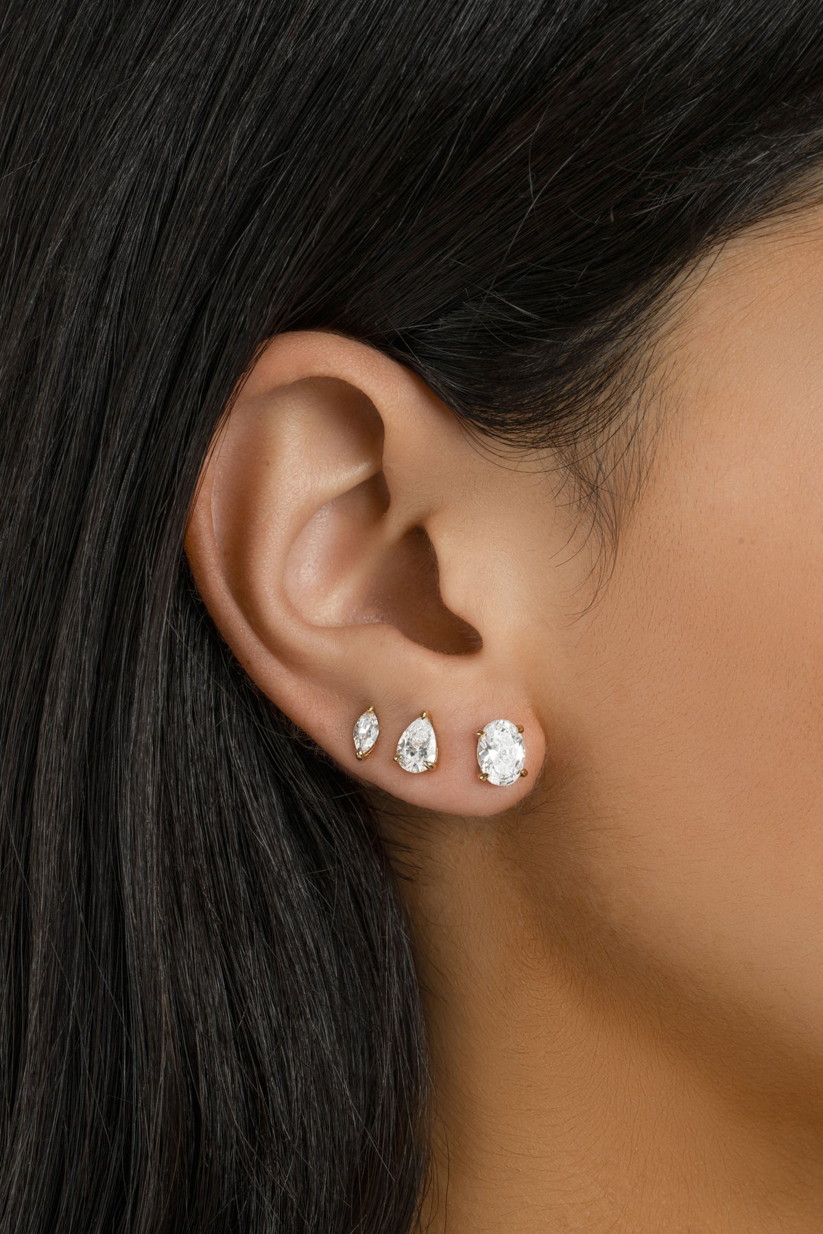 Dark-haired model wearing a graduated stack of three oval studs.