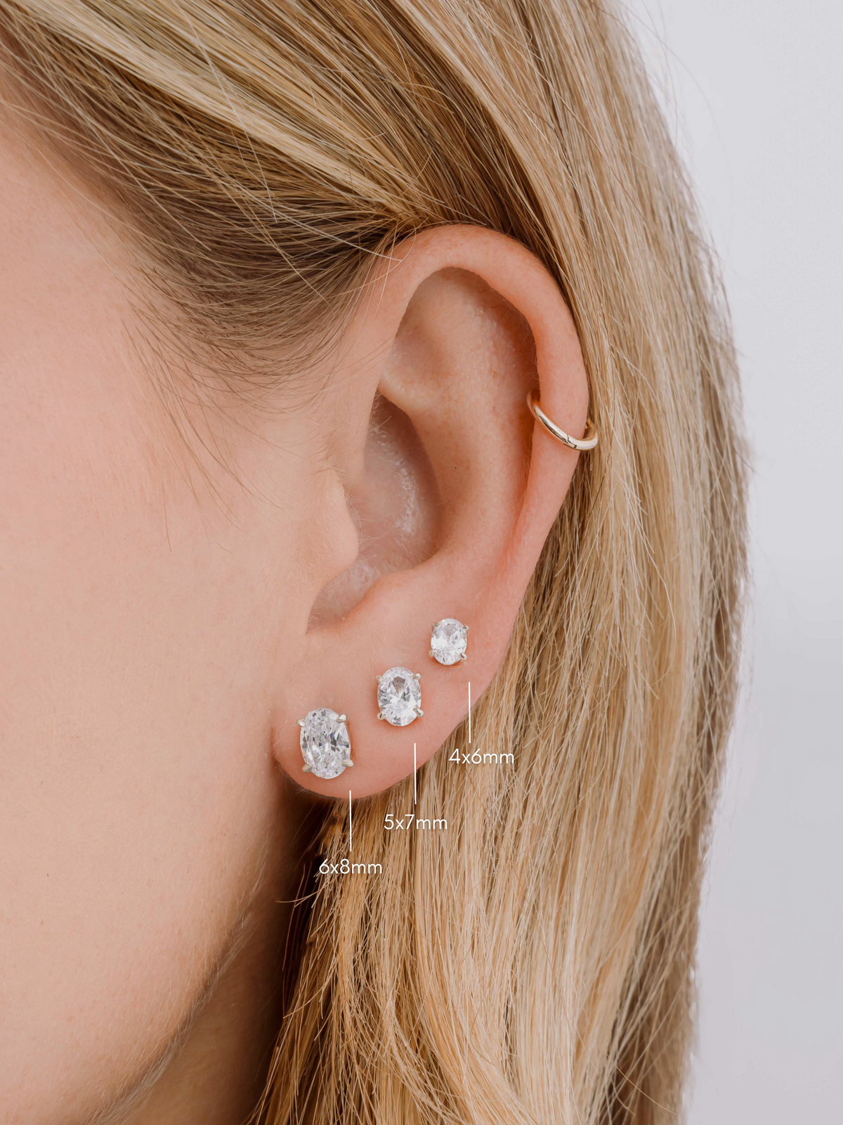 Silver oval studs in three sizes worn together on a model's ear.