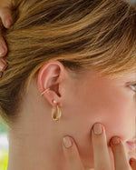 Gold oval textured hoop earrings from Sami Jewels worn by a model, showcasing their stylish and elegant design.