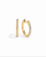 Gold 11mm pavé diamond huggie earrings by Sami Jewels with sparkling diamond details on a white background.