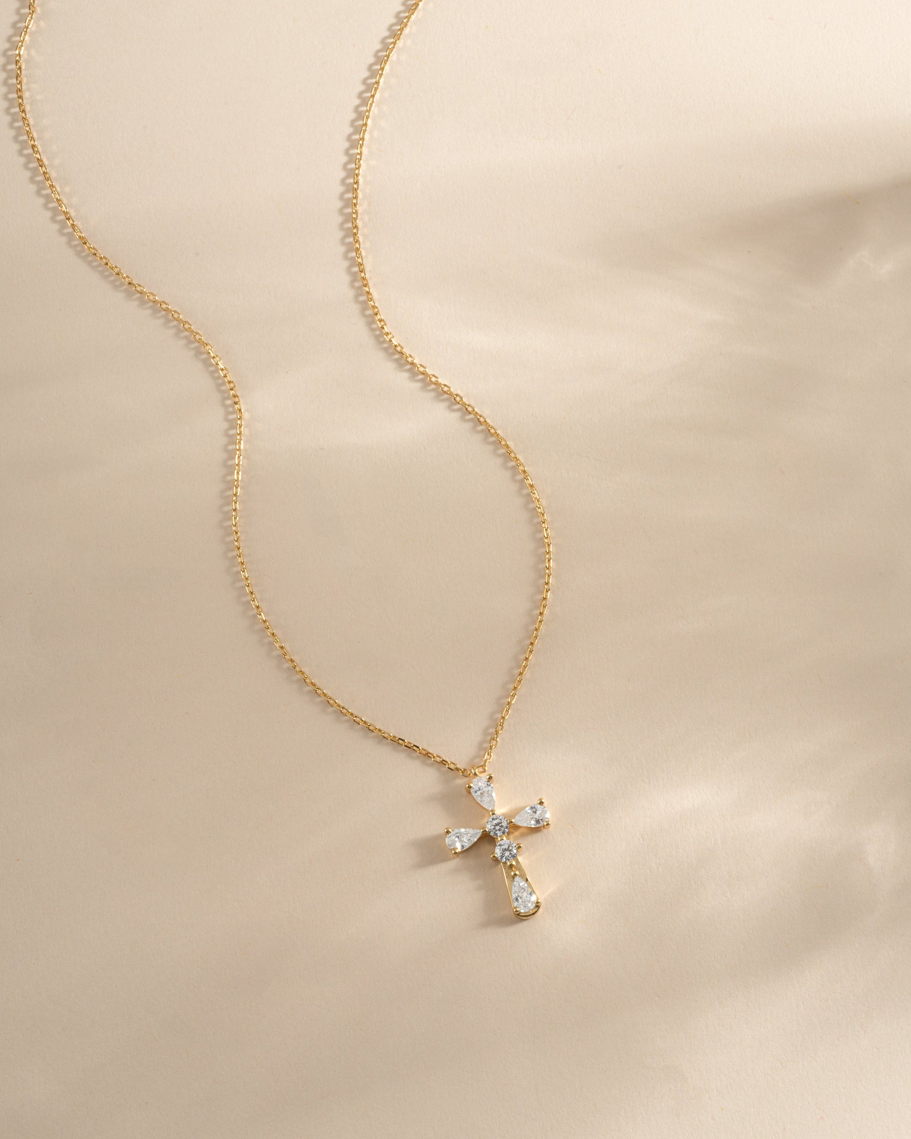 Gold pear-cut cross necklace by Sami Jewels displayed on a white background. Elegant jewelry piece with a detailed cross pendant.