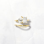 A toi et moi diamond ring with a dainty gold matching band on a white background