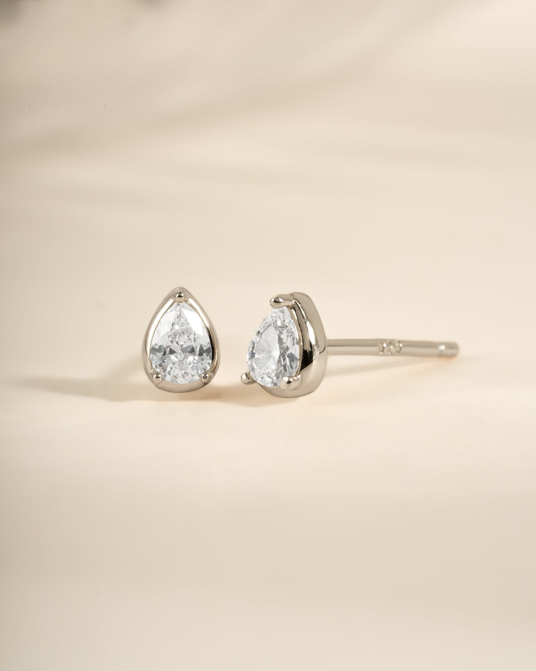 Sterling silver Tiny Pear Stud Earrings by Sami Jewels displayed from an angled view, showcasing their small pear shape and shiny finish.