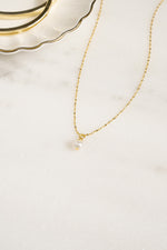 Gold pearl pendant necklace with a single pearl charm, designed by Sami Jewels, shown from an angled view.