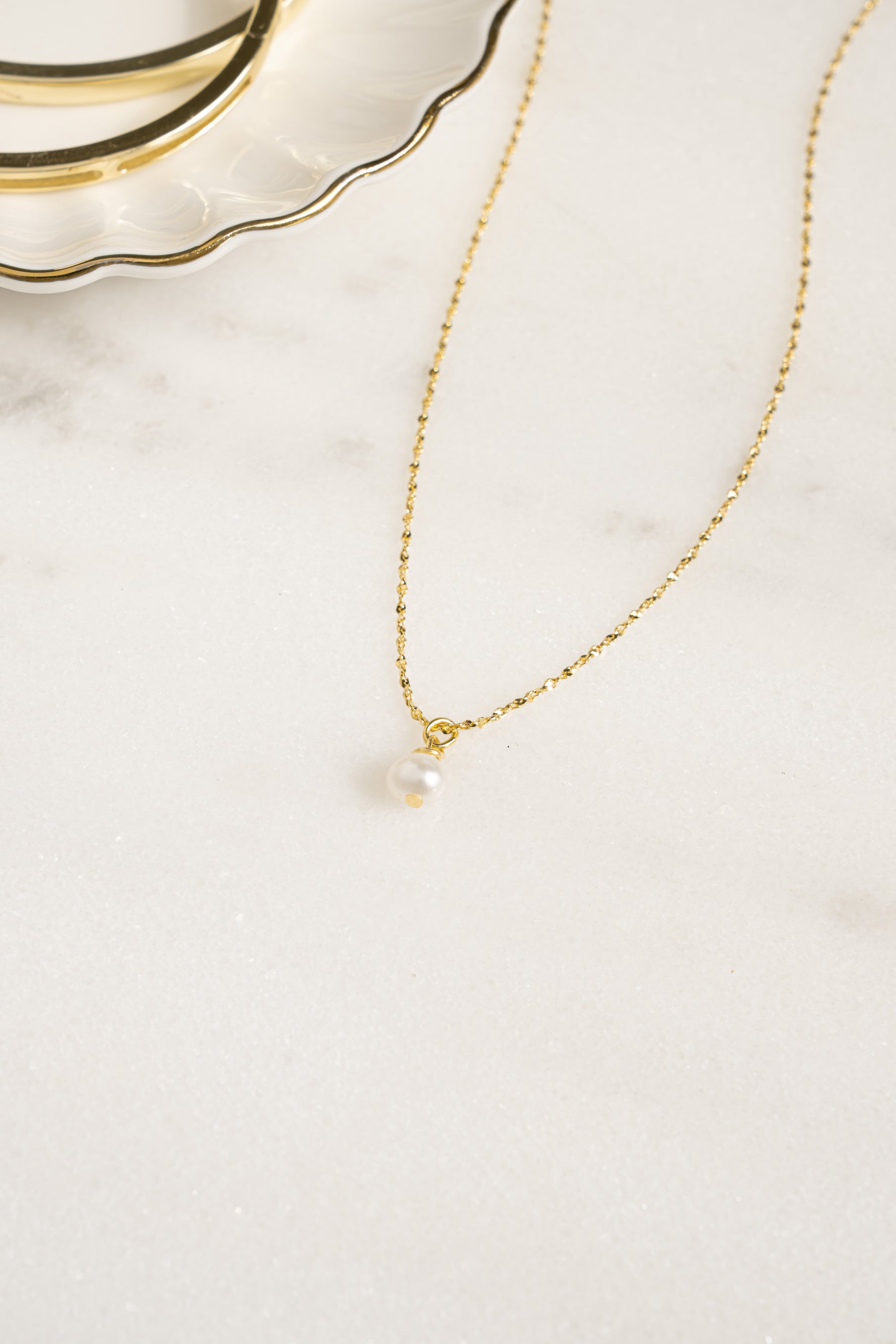 Gold pearl pendant necklace with a single pearl charm, designed by Sami Jewels, shown from an angled view.