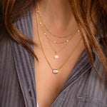 model wearing Bezel Emerald Cut Necklace layered with delicate gold chains, creating a trendy stacked jewelry look. 