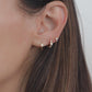 A closeup video of a model wearing two baby hoop earrings and one stud earrings. In the first piercing she is wearing huggie hoop earrings, in the second is another small opal earring with diamonds, and in the third is a tiny opal stud earring. 