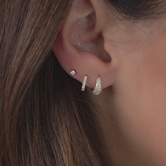 Video of model wearing 3 earrings including a pave diamond huggie earring, diamond huggie hoop earring, and dainty solitaire diamond stud earring.