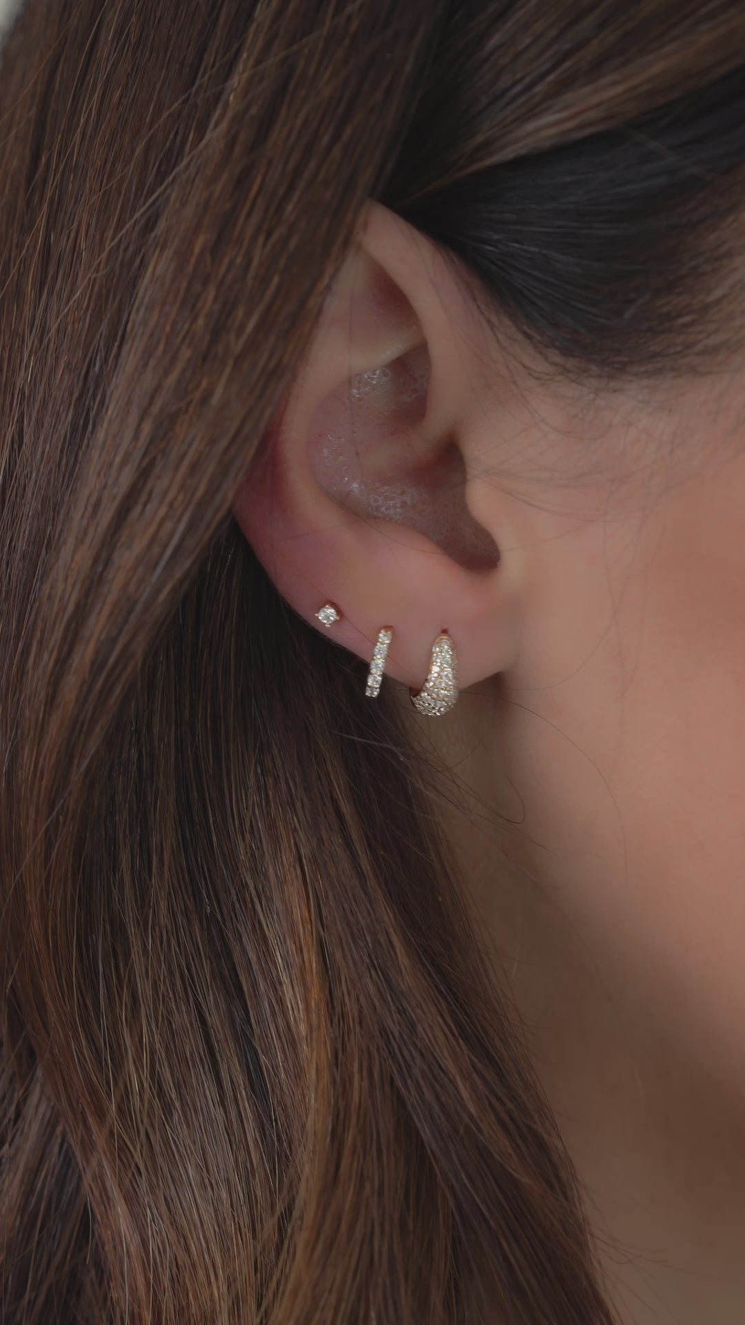 Video of model wearing 3 earrings including a pave diamond huggie earring, diamond huggie hoop earring, and dainty solitaire diamond stud earring.