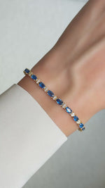 Gold sapphire cubic zirconia tennis bracelet with alternating round stones shown in motion on wrist.