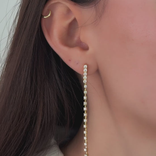 video of model wearing long earrings in gold featuring shimmering diamonds that feel smooth yet structured, perfect as statement earrings.