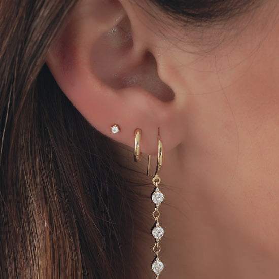 Video of woman wearing 3 gold diamond earrings, a cz diamond drop earring, simple gold huggie hoop, and tiny diamond stud earring.