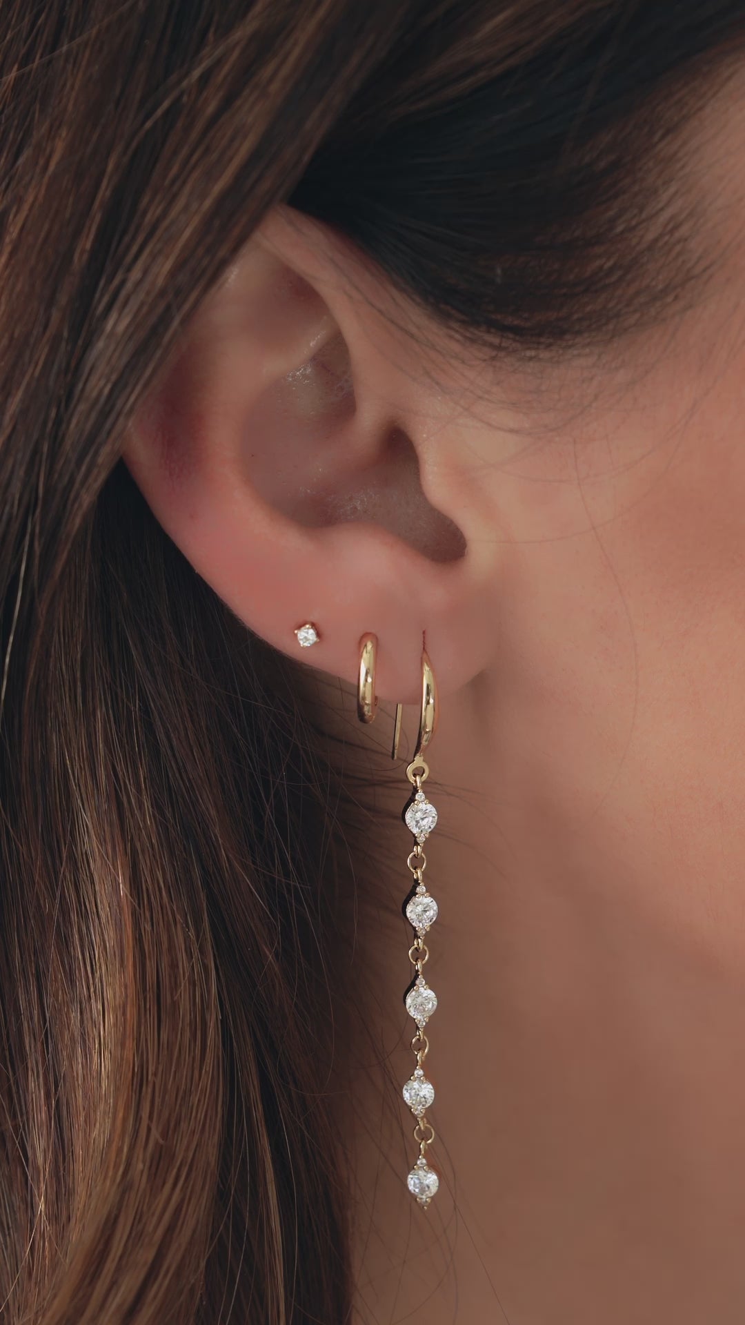 Video of woman wearing 3 gold diamond earrings, a cz diamond drop earring, simple gold huggie hoop, and tiny diamond stud earring.