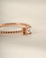 Close-up of a Sami Jewels rose gold princess cut ring with a beaded band design on a white background.