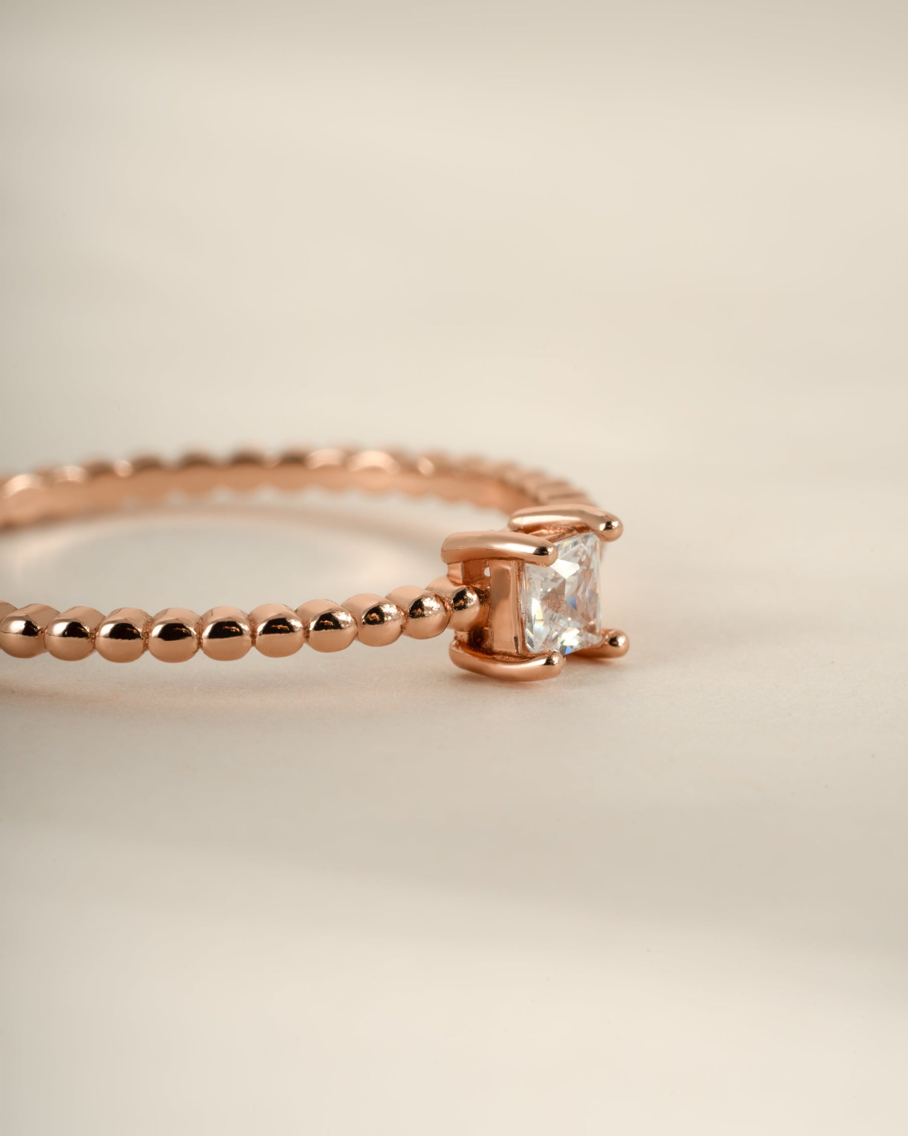 Close-up of a Sami Jewels rose gold princess cut ring with a beaded band design on a white background.