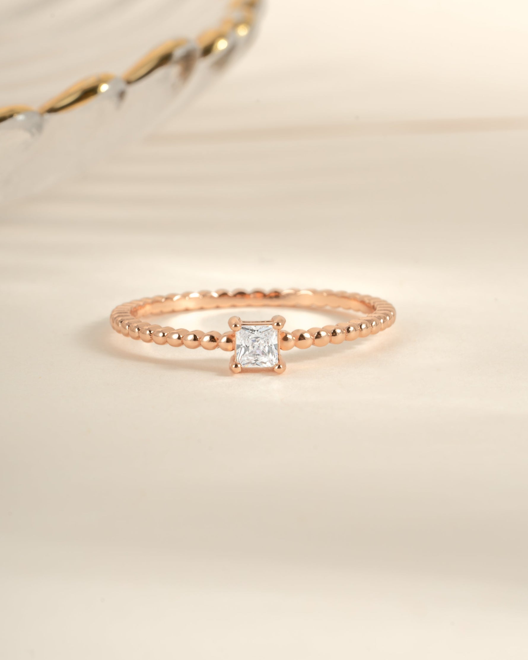 Rose gold princess cut ring with a beaded band from Sami Jewels, showcasing a sparkling central gemstone and intricate band detail.