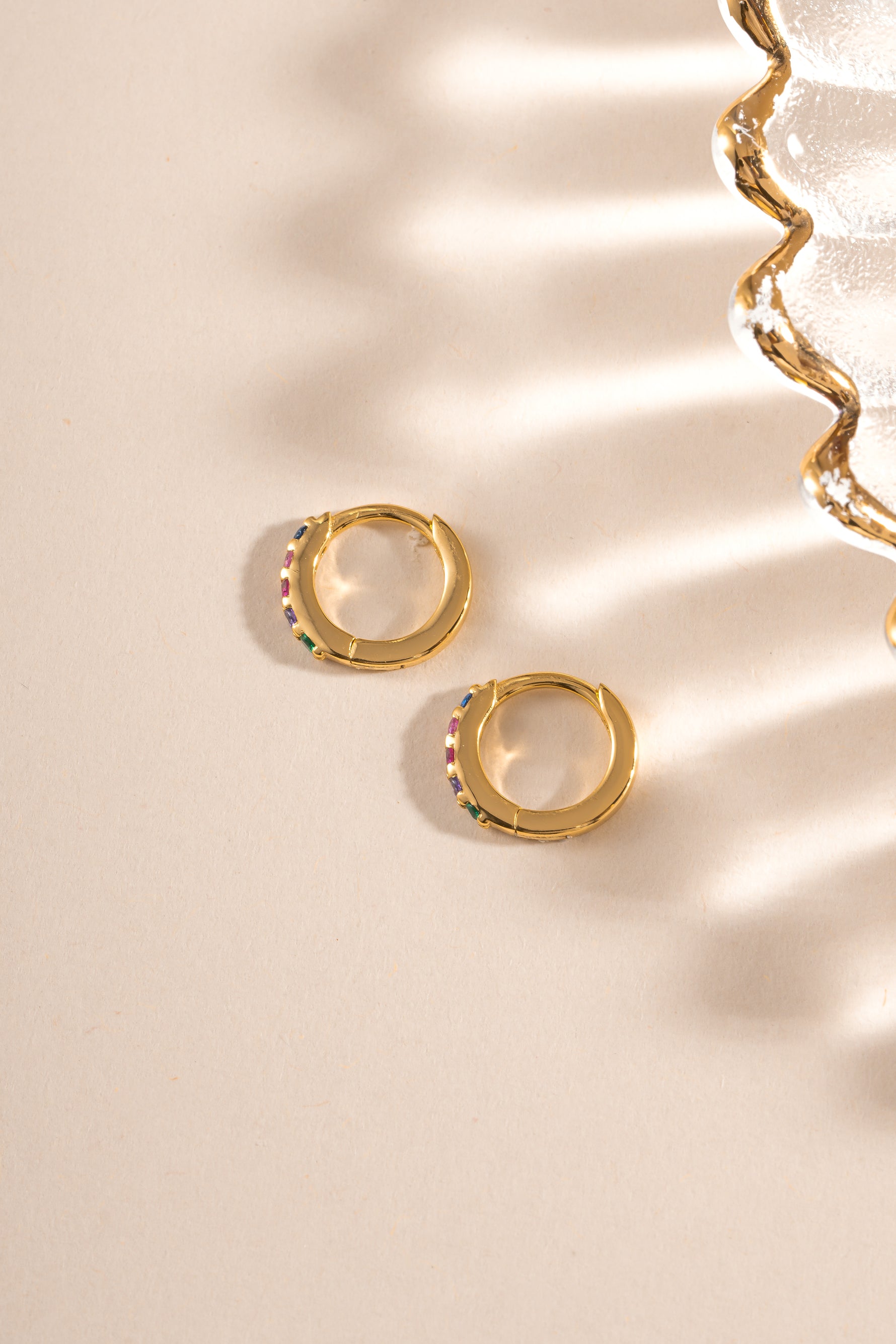 Gold 7mm rainbow studded huggie earrings by Sami Jewels shown in side profile view.