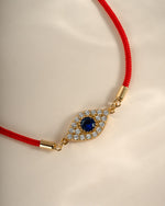 Close-up of Sami Jewels red string evil eye bracelet with a prominent blue and white evil eye charm on a red string.