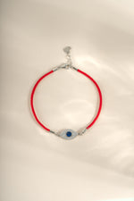 Red string evil eye bracelet with sterling silver charm from Sami Jewels, featuring a vibrant evil eye design and adjustable string.