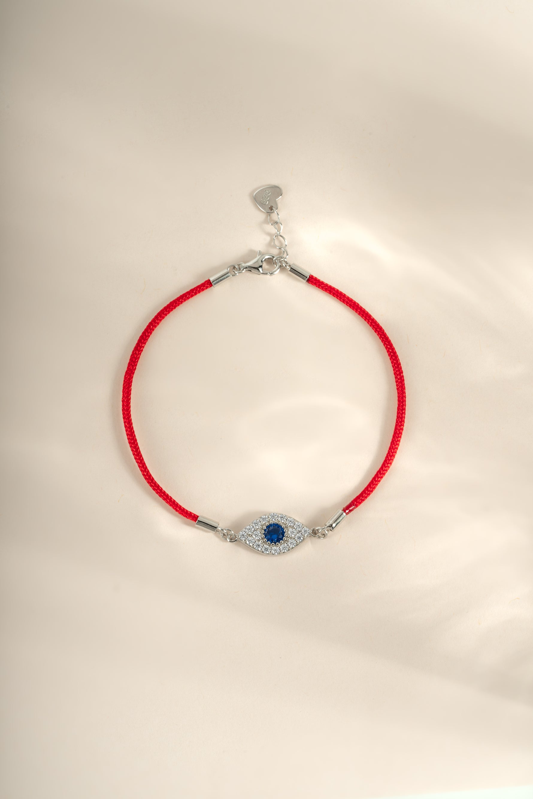 Red string evil eye bracelet with sterling silver charm from Sami Jewels, featuring a vibrant evil eye design and adjustable string.