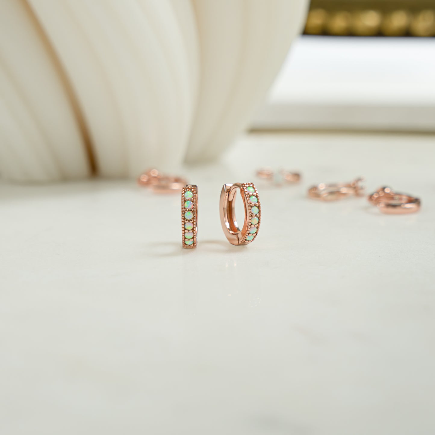 Close up image of tiny opal rose gold tiny hoop earrings. The opal huggie earrings are a dainty and a pretty birthday gift idea.