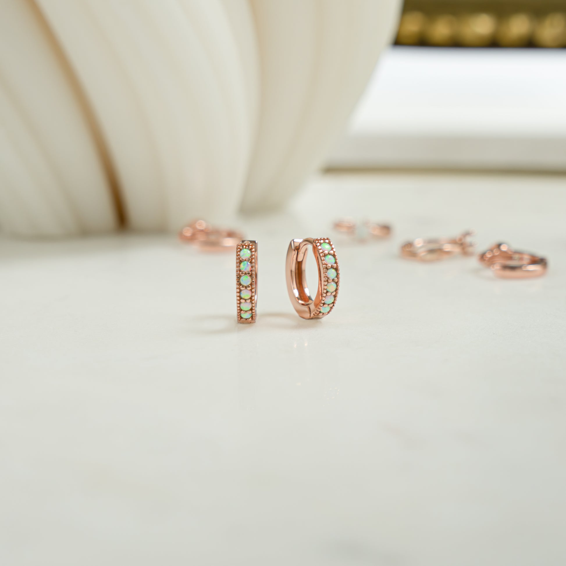 Close up image of tiny opal rose gold tiny hoop earrings. The opal huggie earrings are a dainty and a pretty birthday gift idea.