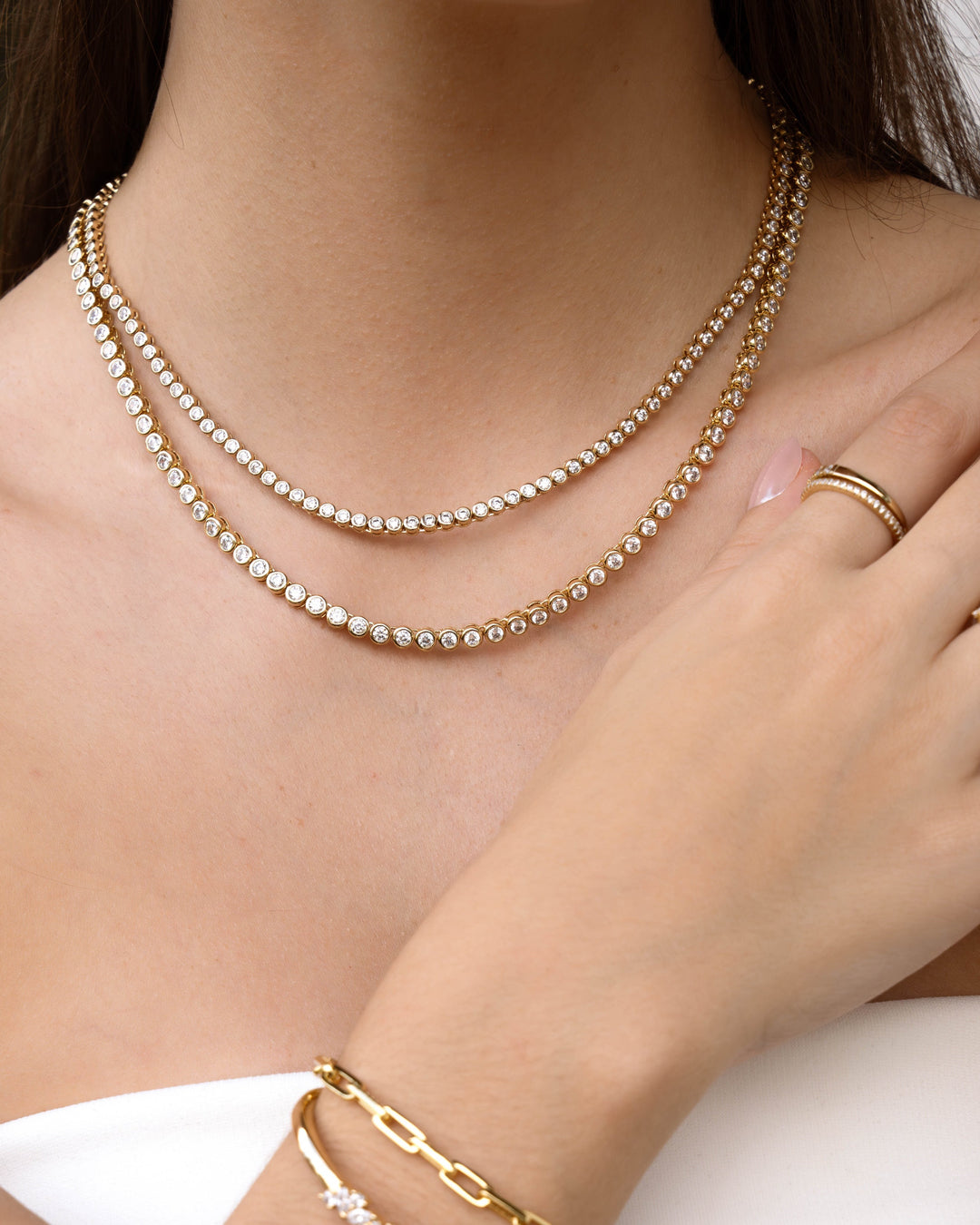 Gold Sami Jewels round bezel diamond tennis necklace stacked with other jewelry, worn by a model.
