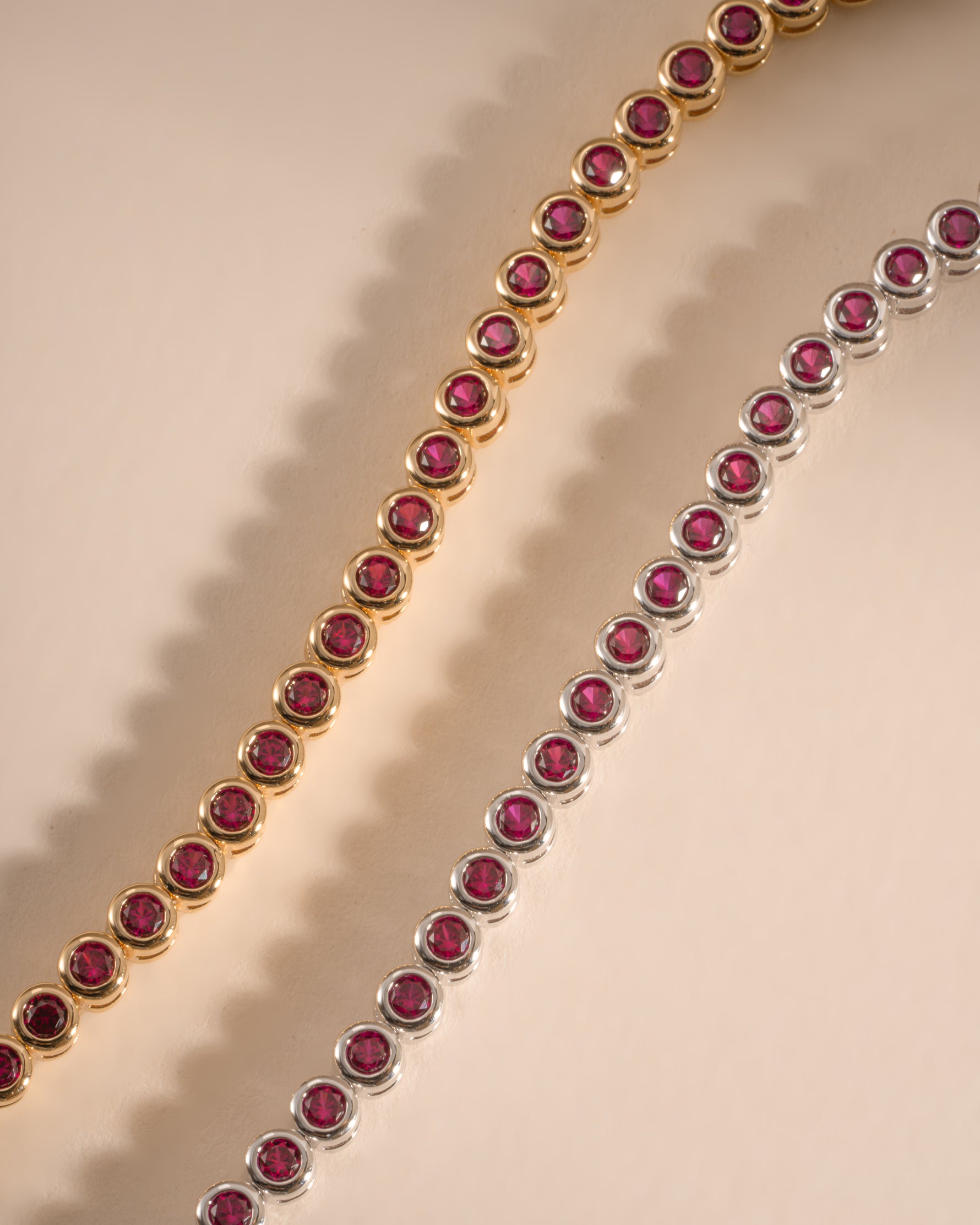 Sami Jewels Ruby Bezel Tennis Bracelet in gold and silver finishes, featuring a row of sparkling rubies in a sleek, elegant design.