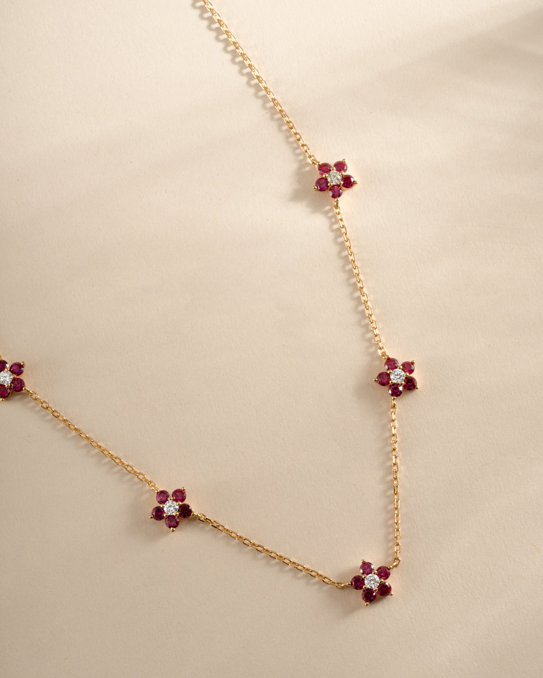 Gold necklace featuring a ruby flower charm from Sami Jewels, showcasing a delicate floral pendant design.