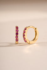 Gold 7mm Ruby Huggies earrings by Sami Jewels featuring ruby-studded hoops with an angled view.