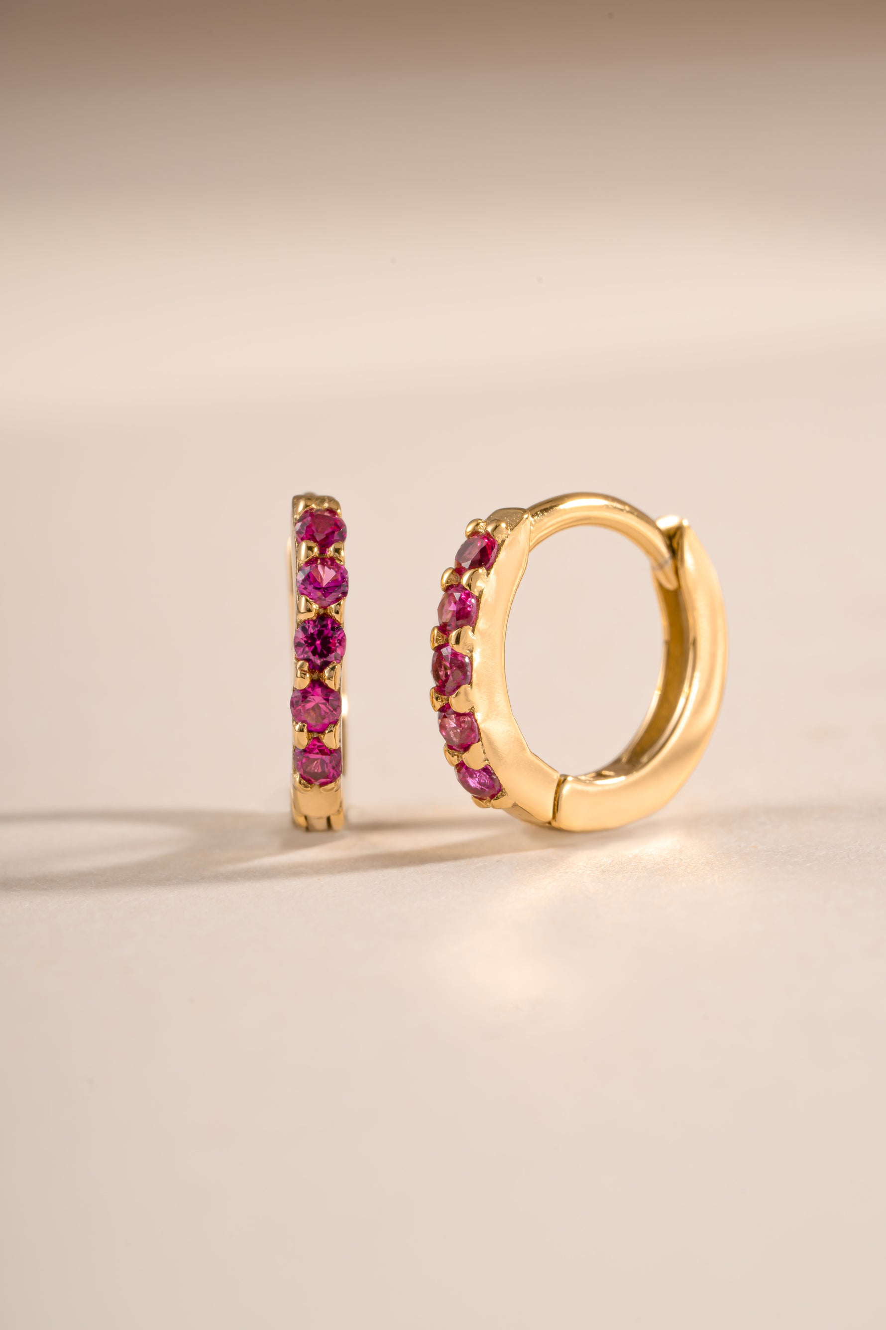 Gold 7mm Ruby Huggies earrings by Sami Jewels featuring ruby-studded hoops with an angled view.
