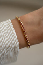 Gold bezel-set Ruby tennis bracelet by Sami Jewels worn on wrist, showcasing vibrant red gemstones and elegant design.