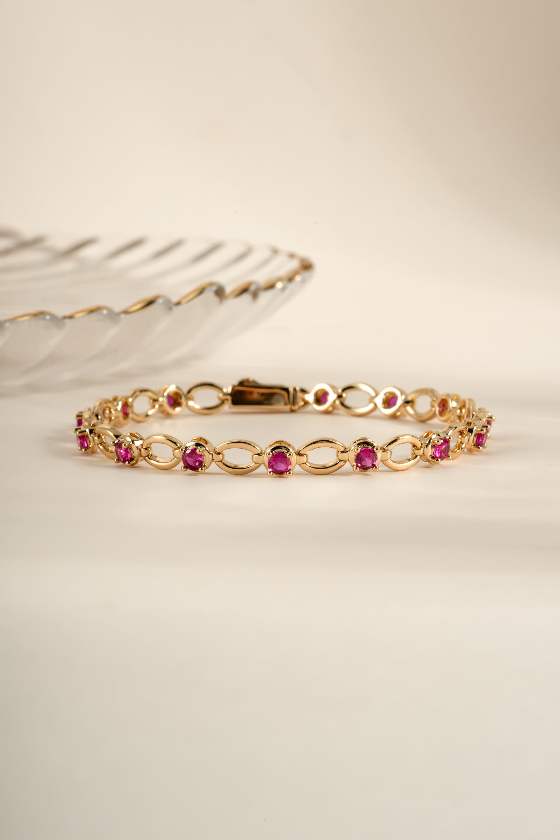 Gold styled flatlay of Sami Jewels Ruby Lilly Tennis Bracelet with sparkling red rubies and gold chain design.