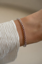 Silver Ruby Bezel Tennis Bracelet by Sami Jewels displayed on wrist with alternating ruby stones set in silver bezel.