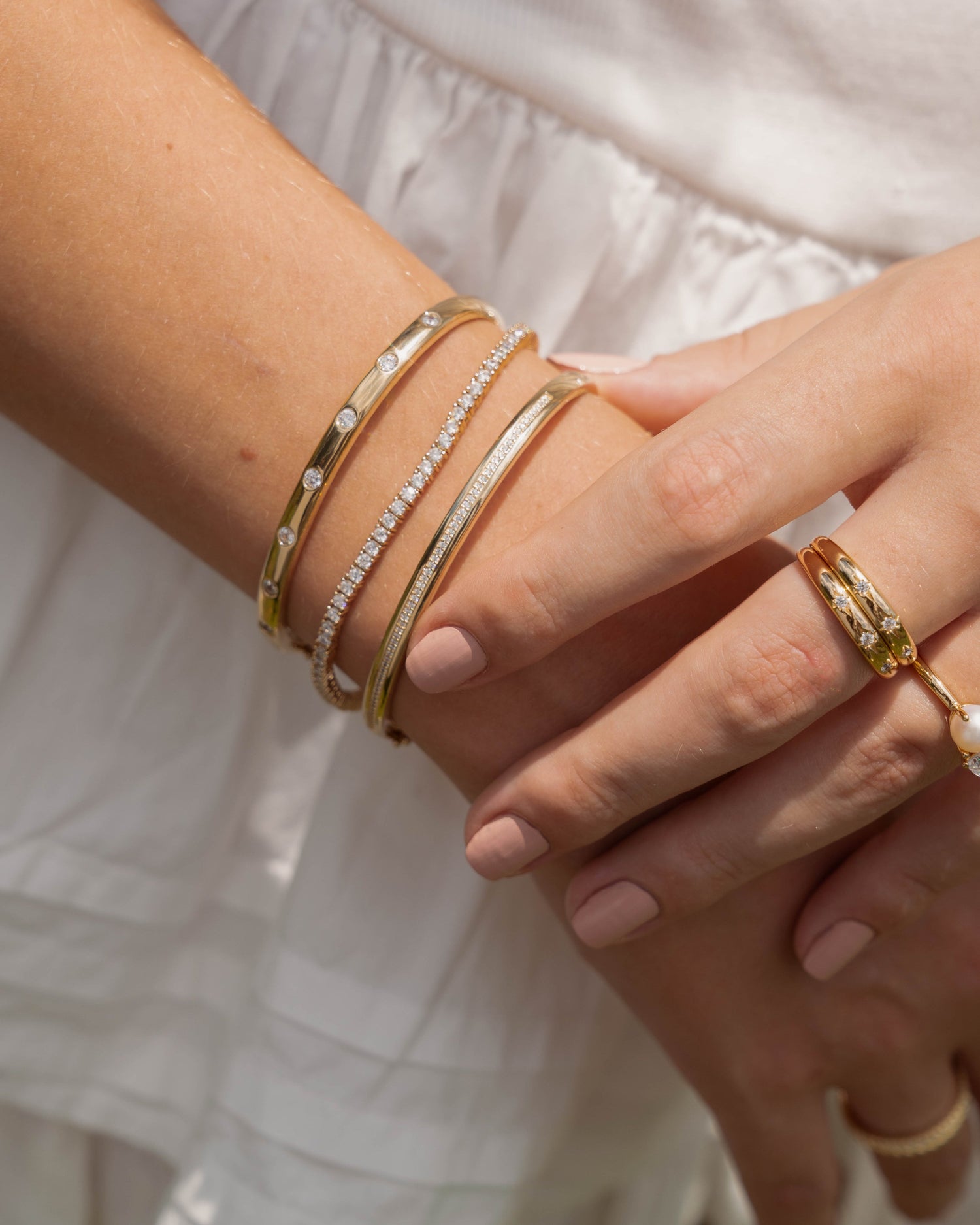 Closeup image of gold bracelet stack featuring a minimalist gold tennis bracelet, a diamond bangle, a bezel set diamond bangle