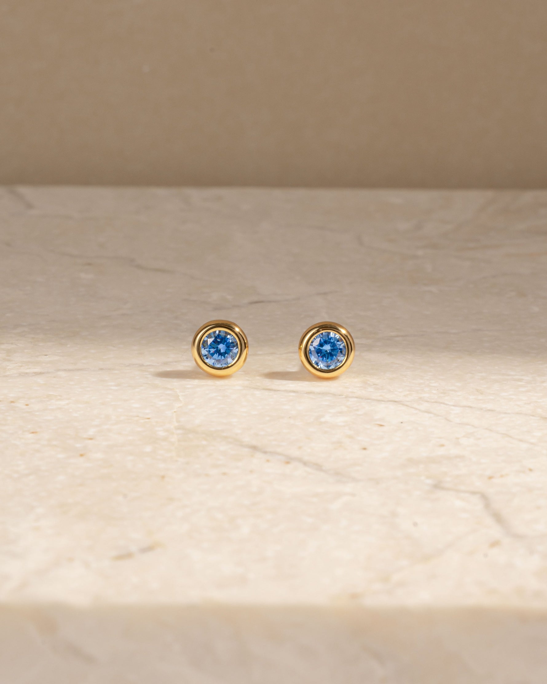 Dainty gold birthstone earrings on a marble background