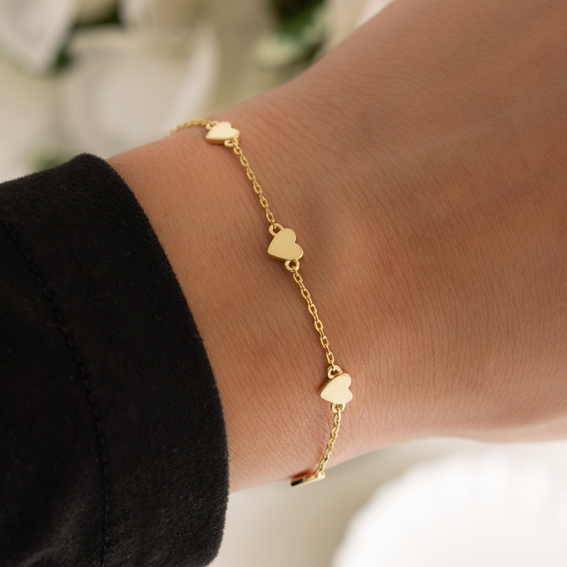 model wearing gold bracelet, highlighting its intricate heart charm details. 